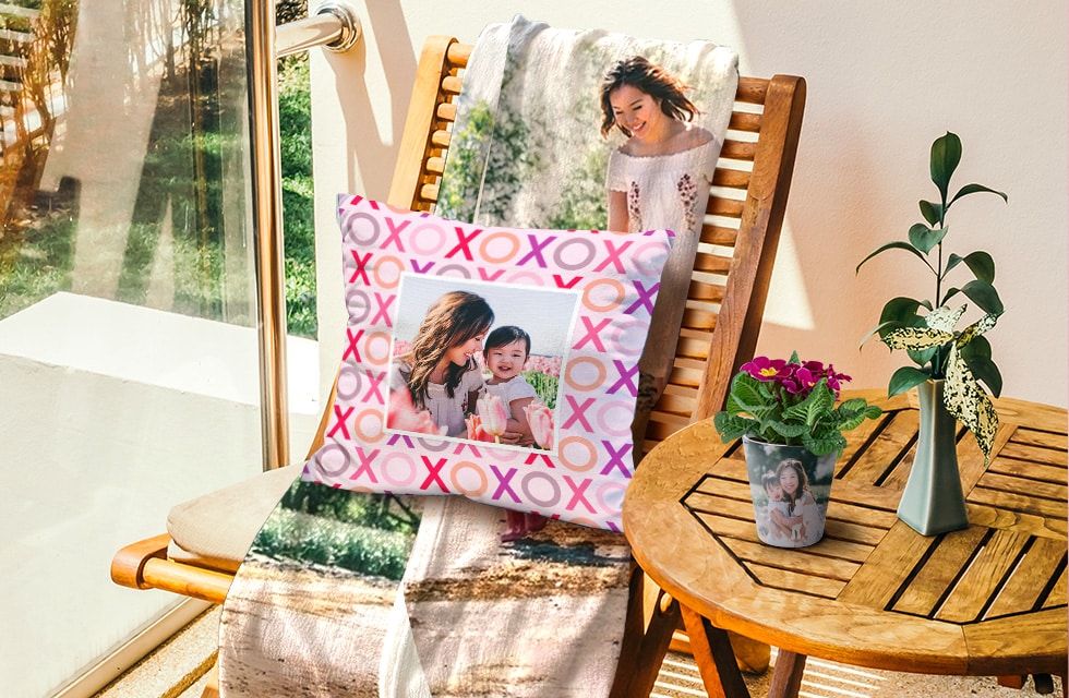Personalised pillow and blanket on a deck chair beside a table with two plants on it.